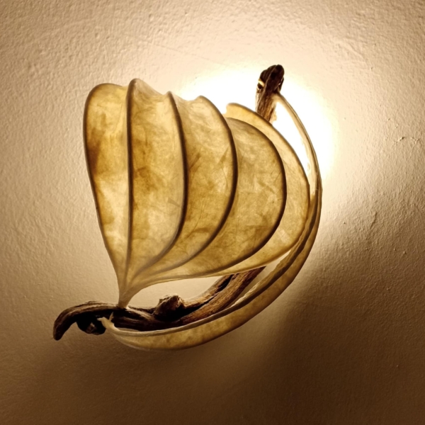 Passage A small wall-mounted light sculpture evoking the gentle form of a vessel in motion. Positioned above the bed, “Passage” emits a soft, ambient glow — a quiet suggestion of movement, memory, and rest. It serves as a luminous marker of transition between day and night, waking and dreaming. Materials: Handmade paper, bamboo, driftwood, fabric-covered electrical wire, porcelain light socket Dimensions: 30 × 25 × 20 cm